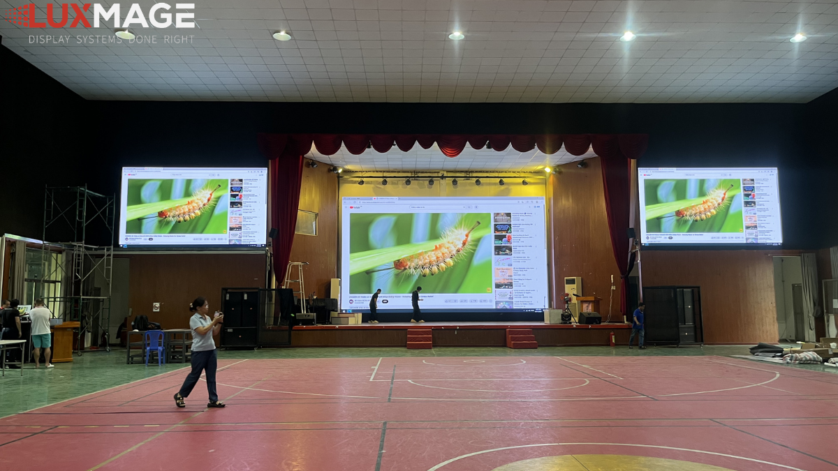 Comparing display quality between LED screens and projectors in an auditorium.